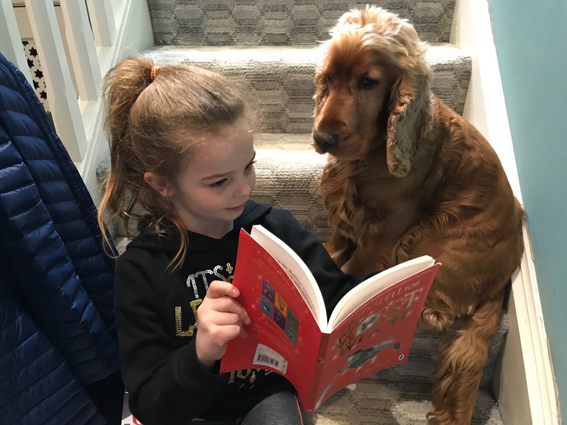Year Two pupil Lara reads a book with her dog for World Book Day